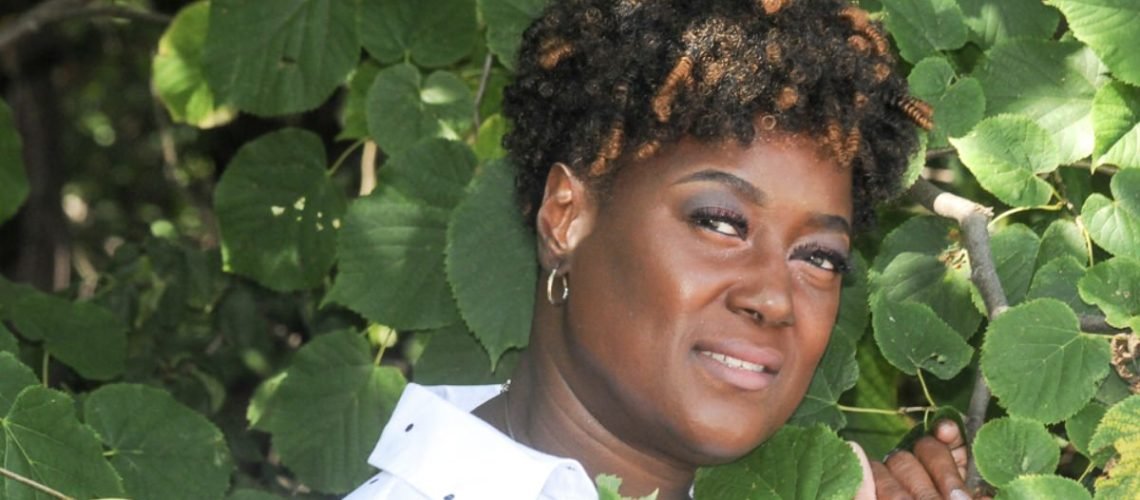 Close up of an African American woman standing next to a tree smiling.